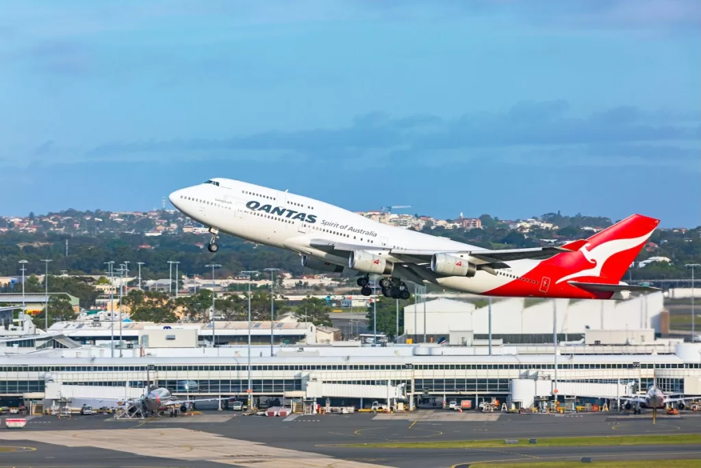 a Qantas 747 taking off from Sydney airport with the terminal building in the background.