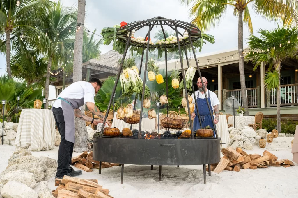Chefs roasting meats and vegetables over a large fire pit