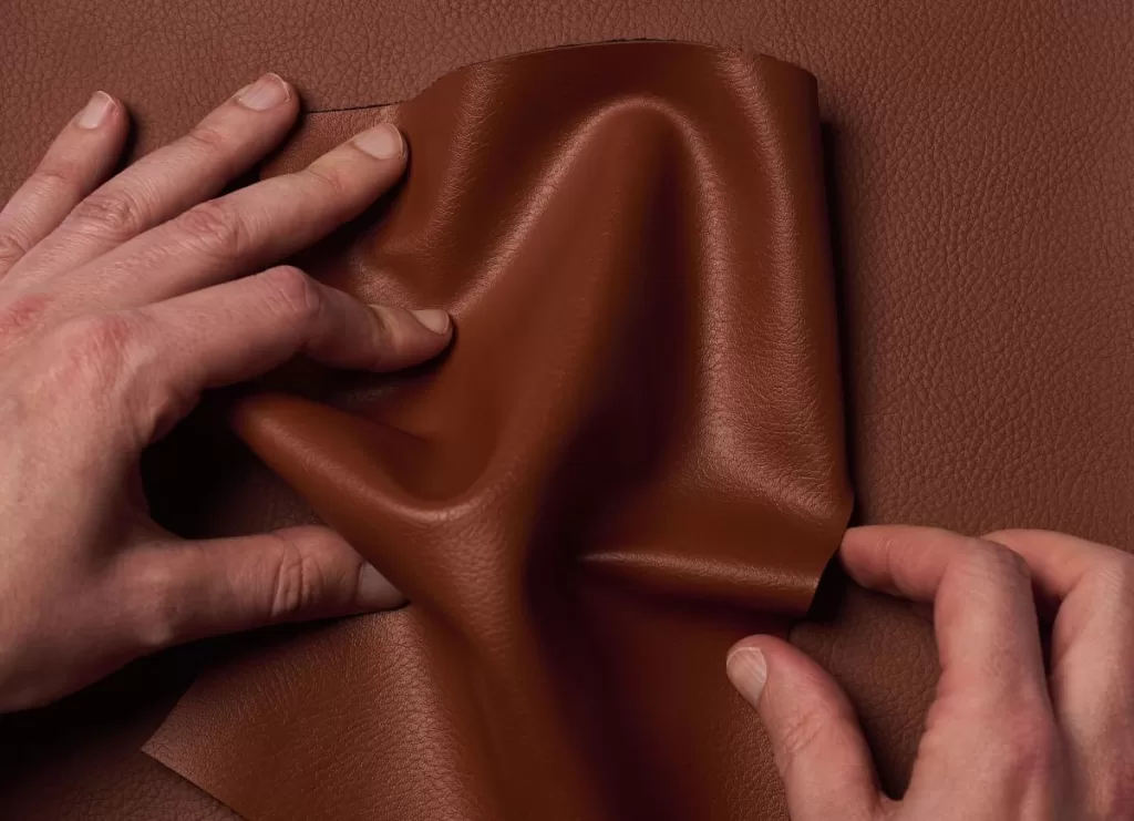 Two hands crumple Uncaged Innovations' artificial leather.
