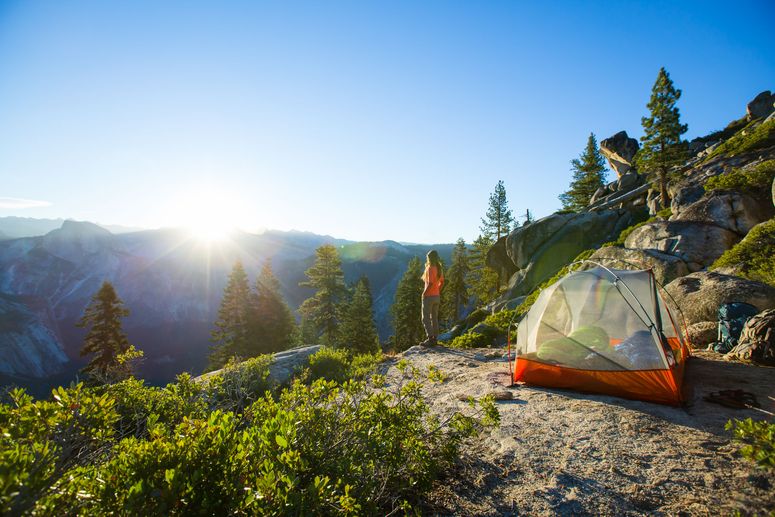 امرأة تتمتع بإطلالة على Half Dome عند شروق الشمس أثناء التخييم في الجبال