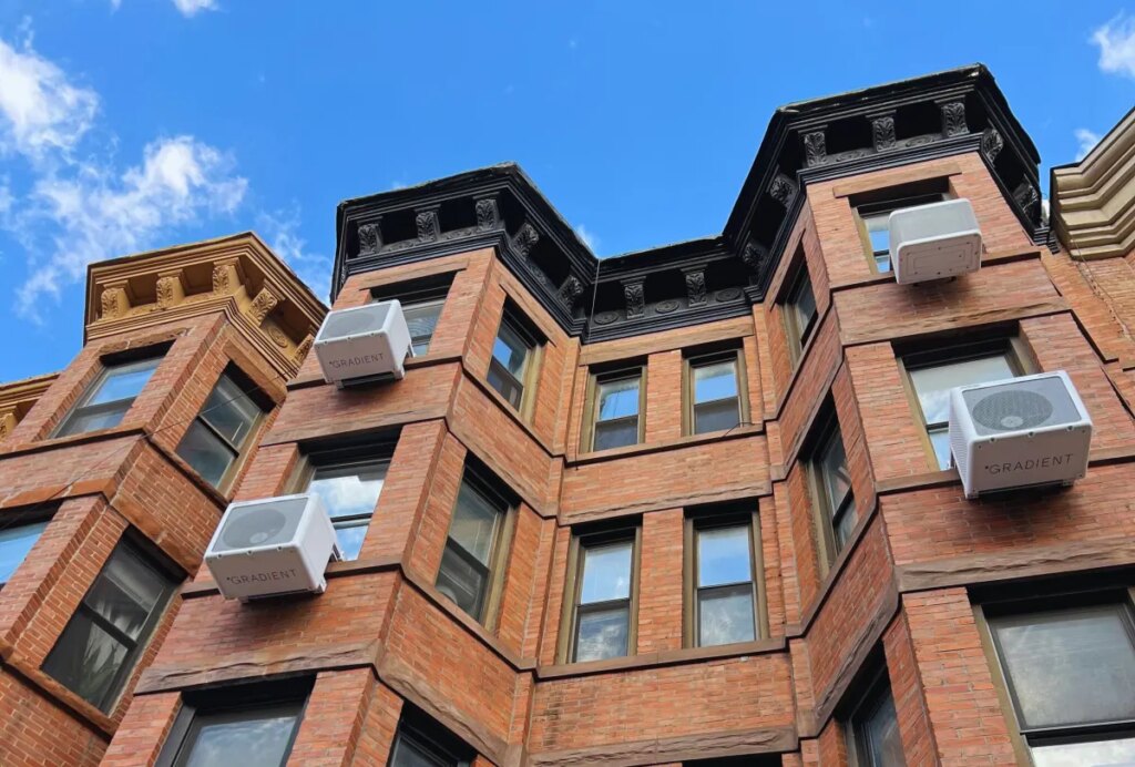 Heat pumps hang on the outside of an apartment building.